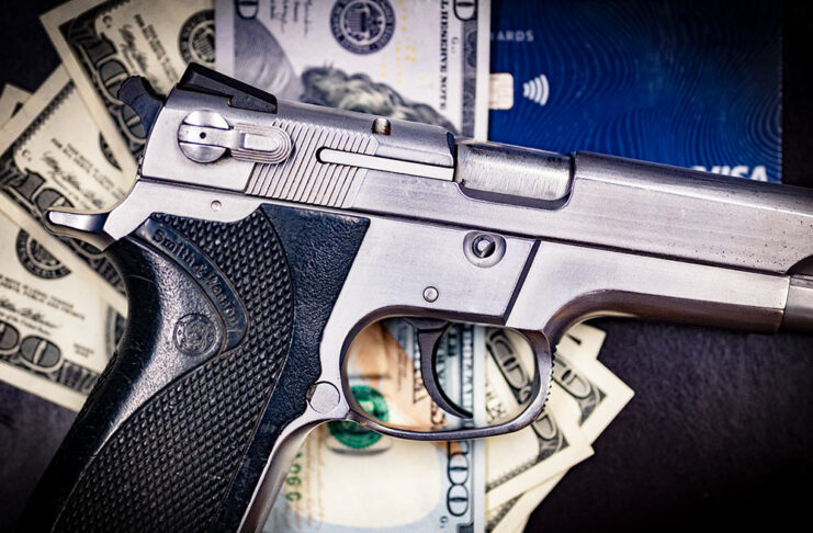 A photo of a handgun with money representing the credit card gun registry scheme. Photo credit to Jim Grant
