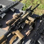 Rifles laying on a wood table outside.