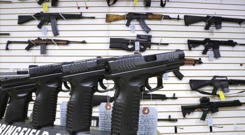 Pistols lined up on a display case and rifles on the wall of a gun store.