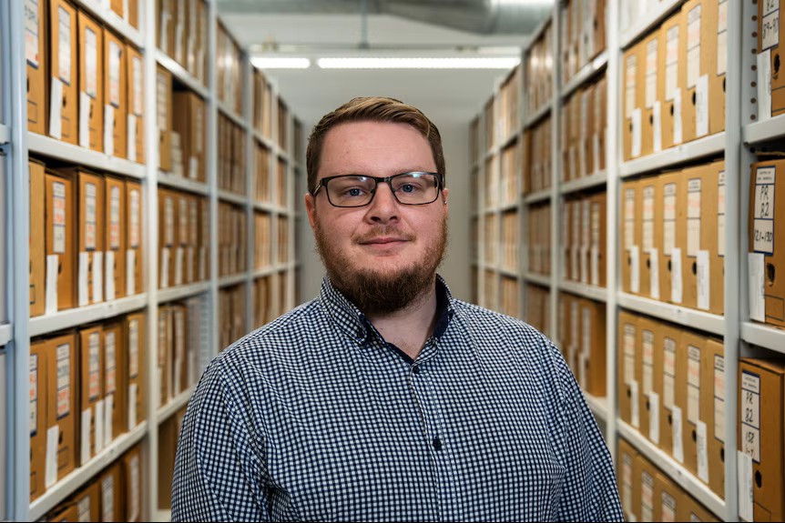 Man with glasses stands in front of filing shelves